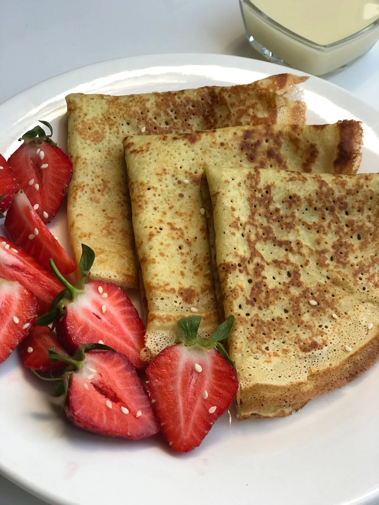 A plate of crepe and strawberries with dip on the side