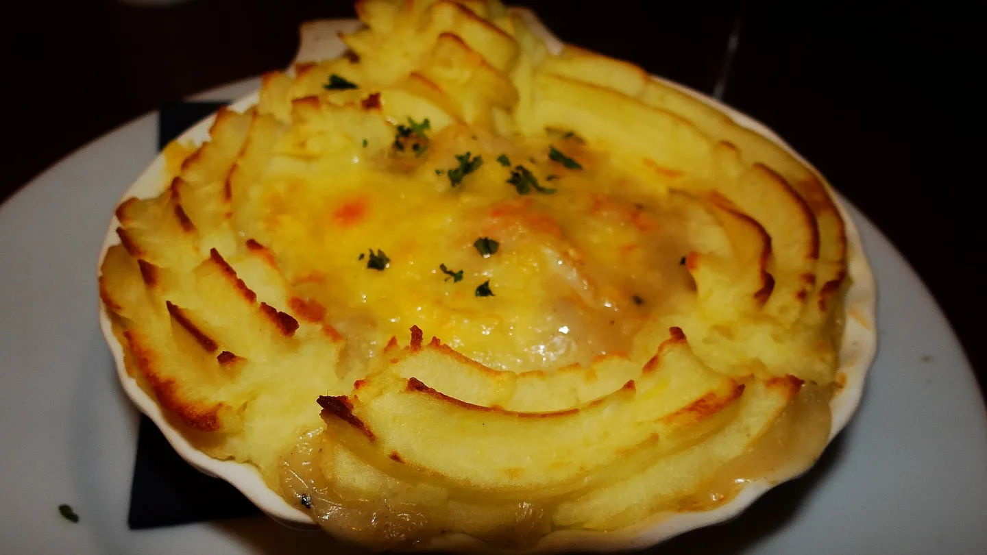 A scallop gratin served in a shell with a piped potato border.