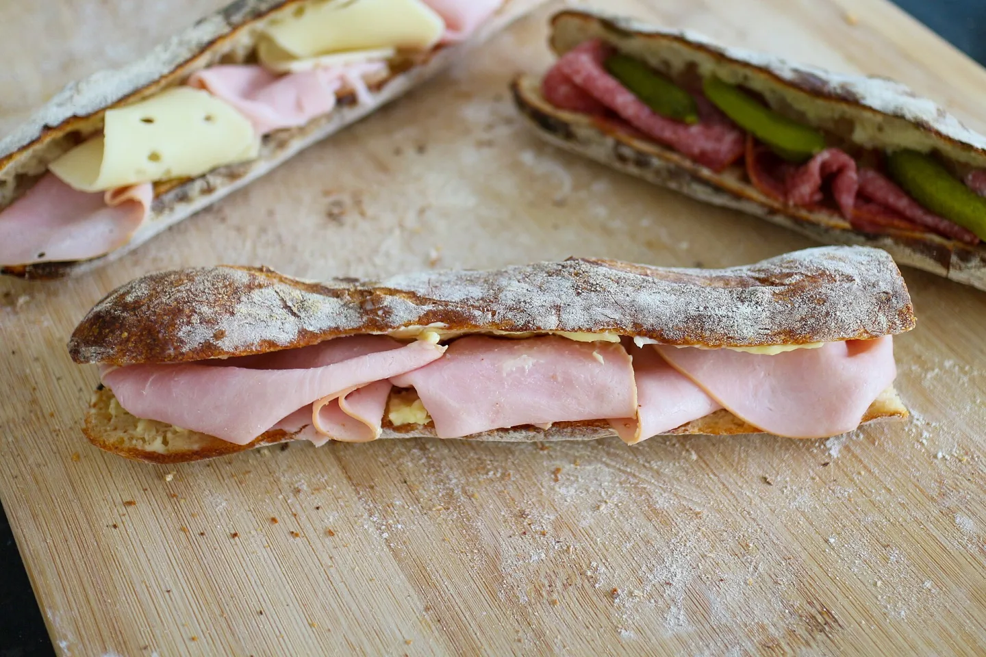 A ham-and-butter baguette in the foreground, with other sandwiches behind it.